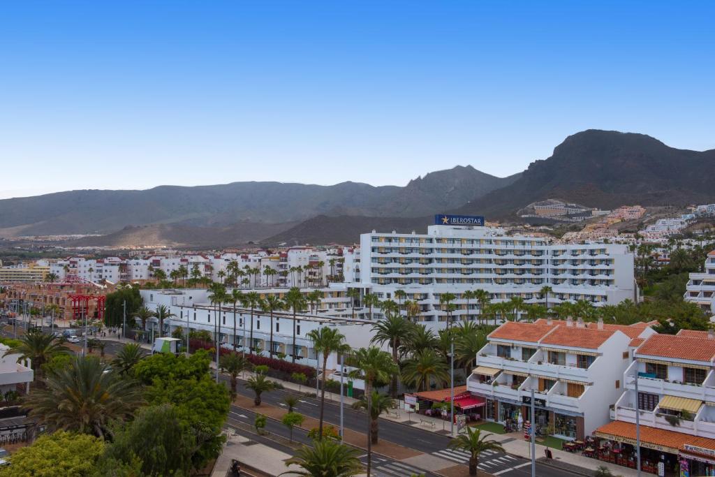 Viesnīcas "Iberostar" ēka ar palmām un kalniem fona. Skaidrs debesis un mierīga pilsētas ainava.
