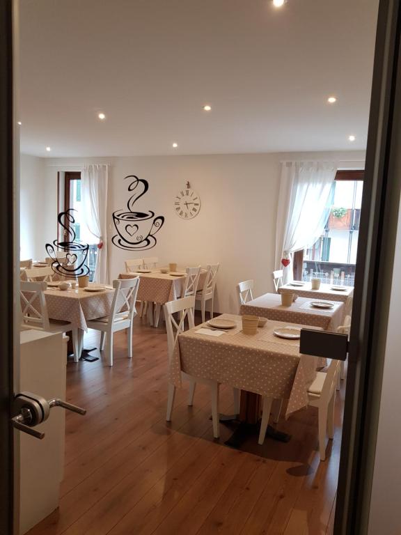 Kafejnīca ar viesmīlīgu interjeru, kurā ir galds ar baltiem galdautiem un dekoratīviem elementiem, piemēram, krūzēm un pulksteni uz sienas. Gaisīga un mājīga atmosfēra ar daudzām logiem un dabīgu apgaismojumu.