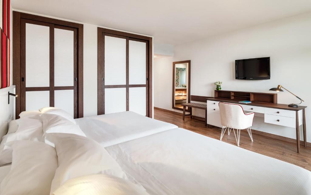 Mūsdienīga guļamistaba ar divām gultām, koka grīdu un elegantu rakstāmgaldu, televizoru un spoguli. Telpa ir gaiša un ērta, piedāvājot mājīgu atmosfēru.