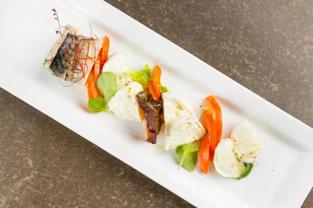 Mūsdienīga pasniegšana ar zivīm, mozzarella sieru un dārzeņiem uz balta šķīvja.