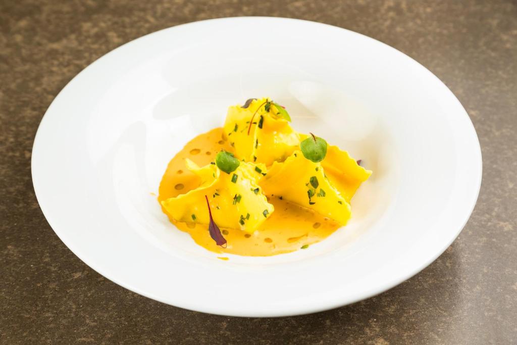 Svaigu ravioli pasniegti uz baltas šķīvja ar dzeltenu mērci un dekoratīviem zaļumiem.