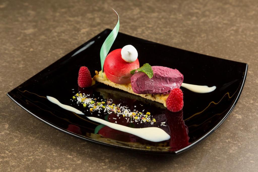 Saldais deserts uz melna šķīvja, kas satur ogu saldējumu, augļu bumbiņu un augu dekorāciju, apvienojot radošu pasniegšanu.
