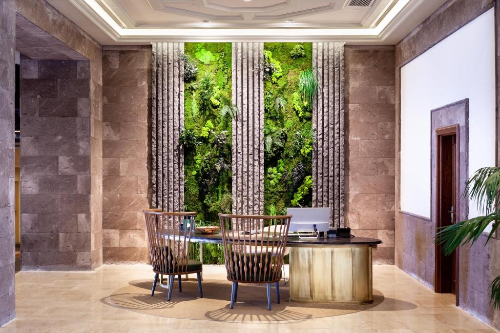 Mūsdienīgs biroja interjers ar zaļu sienu un elegantām mēbelēm, radot relaksējošu atmosfēru. Ideāli piemērots darba vidēm, kas apvieno dabu un komfortu.