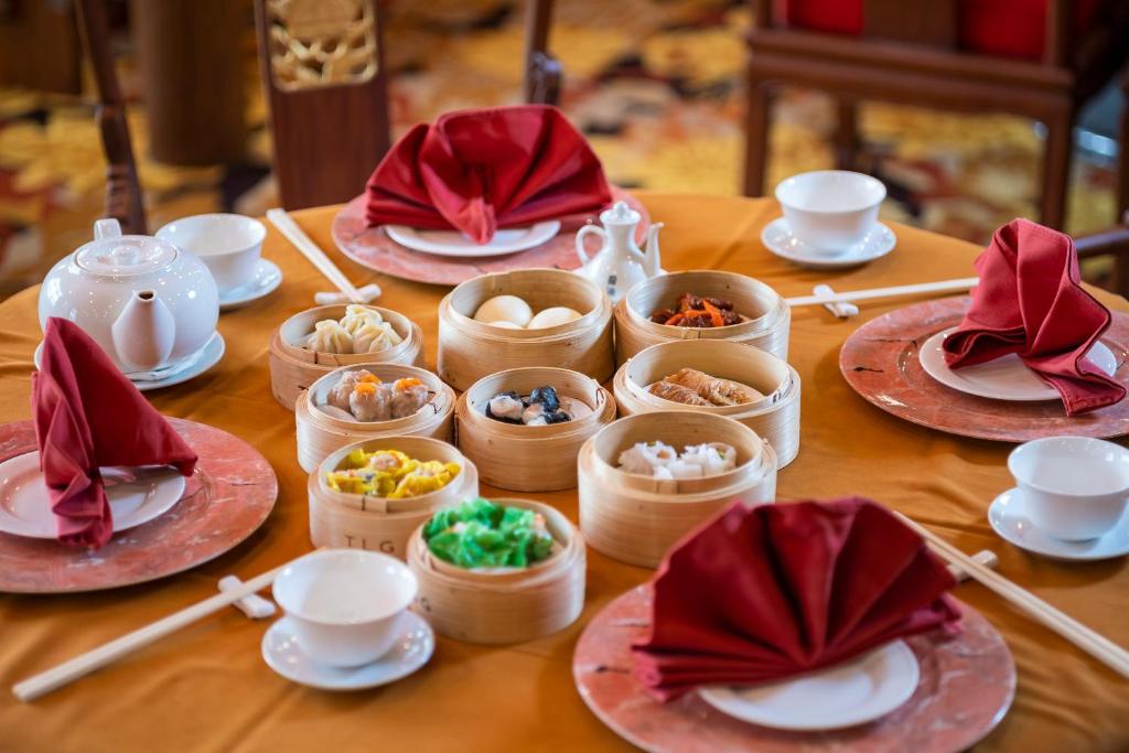 Bagātīgi klāta galda kompozīcija ar dimsum un tradicionālo tēju, kas pasniegta stilīgās bambusa groziņos. Sarkanās salvetes piešķir eleganci un svinīgu noskaņu.