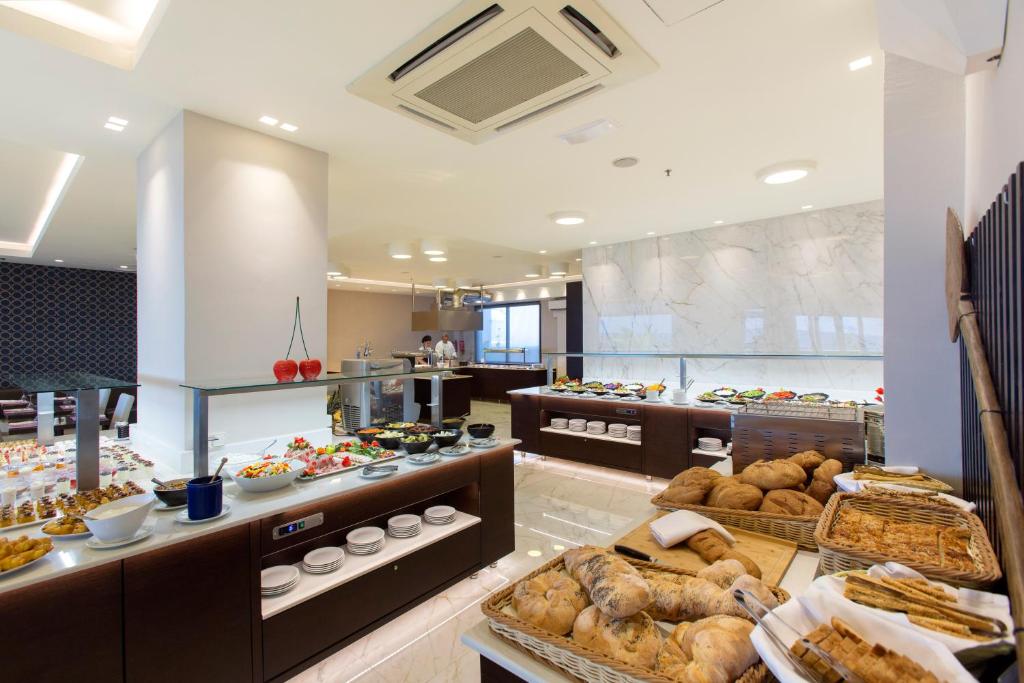 Labi iekārtota brokastu bufete ar dažādām uzkodām, salātiem un maizēm, kas izkārtotas modernā restorānā. Gaisīga atmosfēra un eleganta iekārtojuma detaļas rada patīkamu ēdināšanas pieredzi.