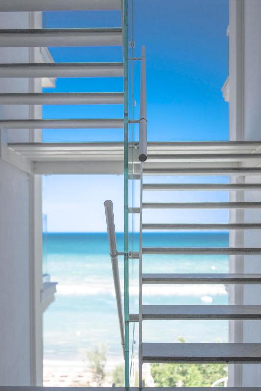 Mūsdienīgas kāpnes ar stikla margām, kas ved uz jūras skatu caur plašu logu. Jūras horizonta zilā krāsa rada mierīgu un relaksējošu atmosfēru.