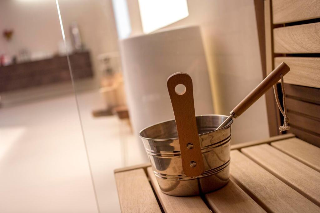 Metāla spainis ar koka rokturi, novietots uz koka soliņa, radot mierīgu un relaksējošu saunas atmosfēru.