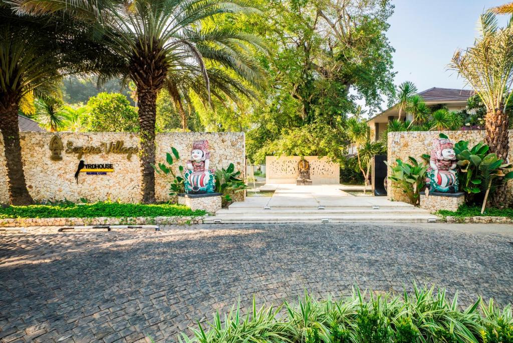 Skaista ieeja "Sugira Village" ar eksotiskām palmām un mākslinieciskām skulptūrām, kas rada unikālu atmosfēru. Ainava ir zaļa un viesmīlīga, ar akmeņainu ceļu un dekoratīvām augu kompozīcijām.