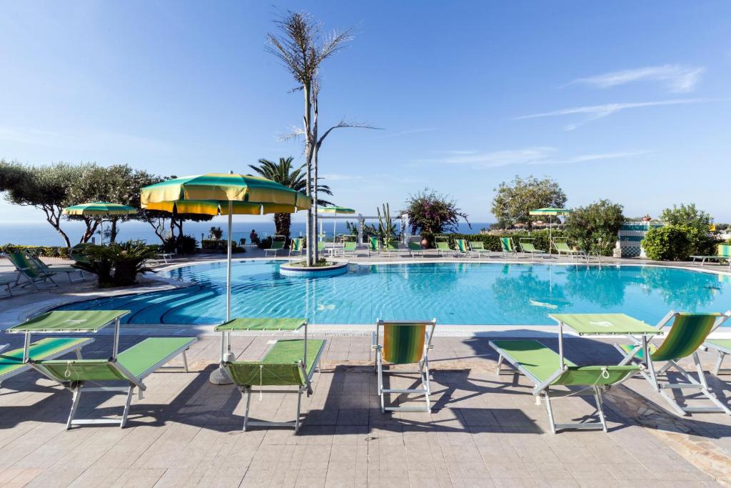 Peldbaseins ar zaļām sauļošanās krēslām un saulessargiem, apkārt dārziem un palmām, piedāvā relaksējošu atmosfēru pie jūras. Skats uz skaidru zilo debesu un ūdens virsmu.