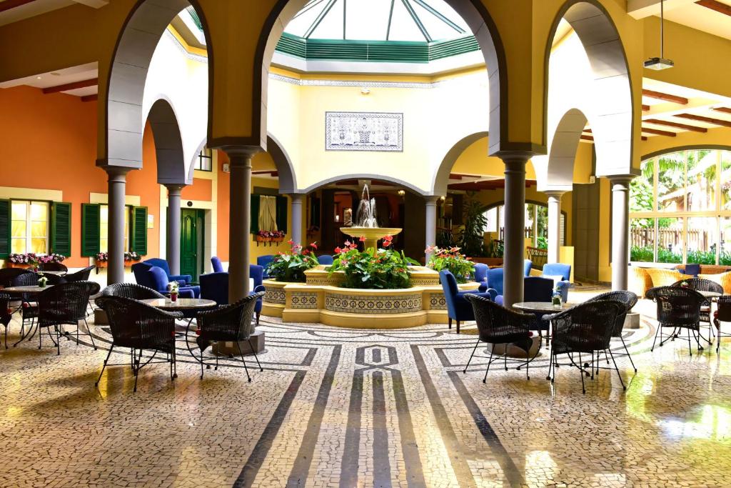 Elegants iekštelpu dizains ar arku elementiem, ūdens strūklaka un zaļumi centrā, kas rada relaksējošu atmosfēru. Sēdvietas ir ērti izvietotas ap zāli, piedāvājot ideālu vietu atpūtai.