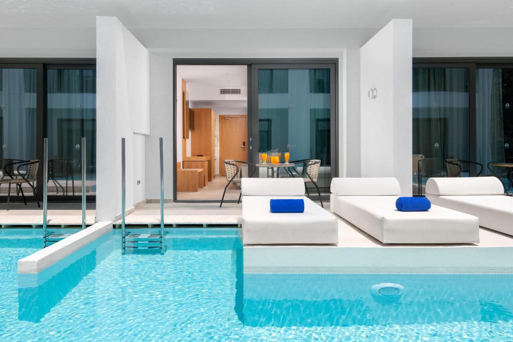 Mūsdienīgs baseins ar baltām sauļošanās gultām un zilu dvieli, kas atrodas pie stiklotām durvīm uz viesistabu. Optimāls relaksācijas un atpūtas vieta.