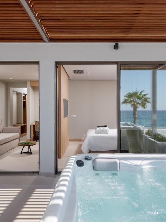 Mūsdienīgs interjers ar burbuļvannu, kas atrodas blakus plašam logam ar skatu uz jūru un palmu. Telpa iekārtota ar gaisīgu un elegantu dizainu.