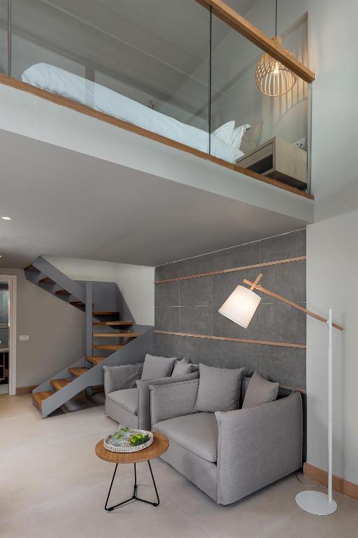 Mūsdienīgs interjers ar divstāvu dzīvojamo telpu, kurā ir gaišas krāsas un moderns dizains. Redzama eleganta kāpne un ērti dīvāni ar kafijas galdiņu.