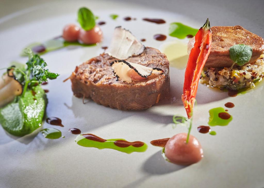 Gurķu un gaļas šķēle uz elegantas plāksnes, papildināta ar zaļumiem un mērci, radot izsmalcinātu gastronomijas pieredzi.