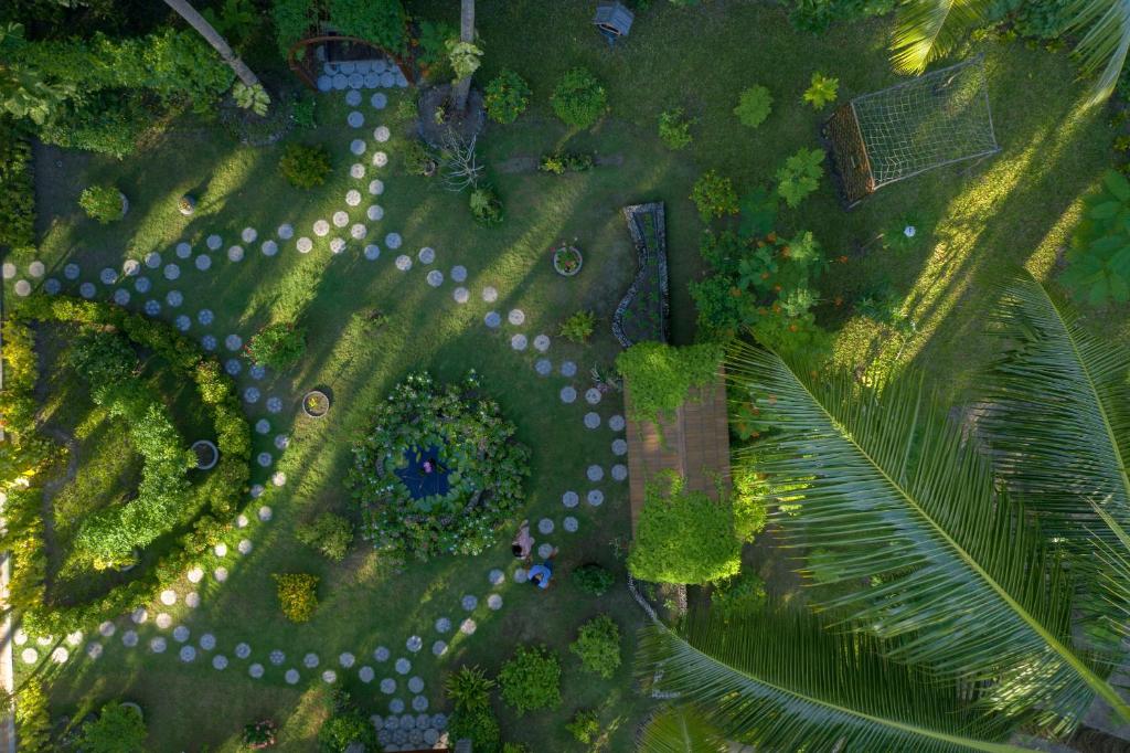 Zaļš dārzs ar akmeņu takām un ziediem, no augšas redzams, ar ainavu, kas ietver ziedu gultas un dārza mēbeles.