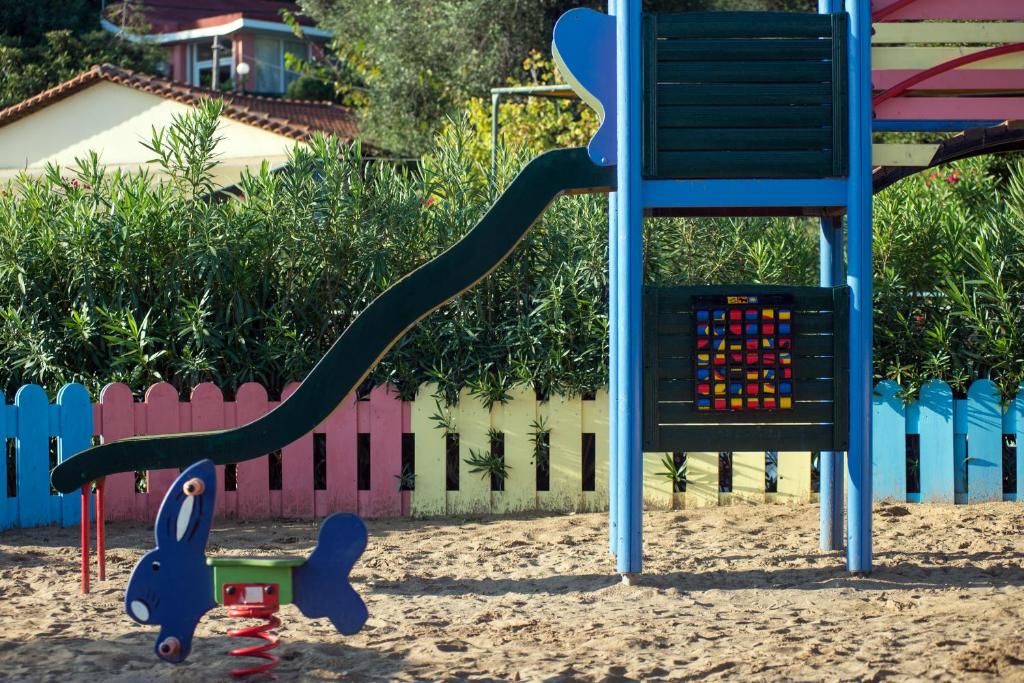 Bērnu rotaļu laukums ar slide un šūpošanos trušu. Apkārt ir krāsaina žoga un zaļa augšana.