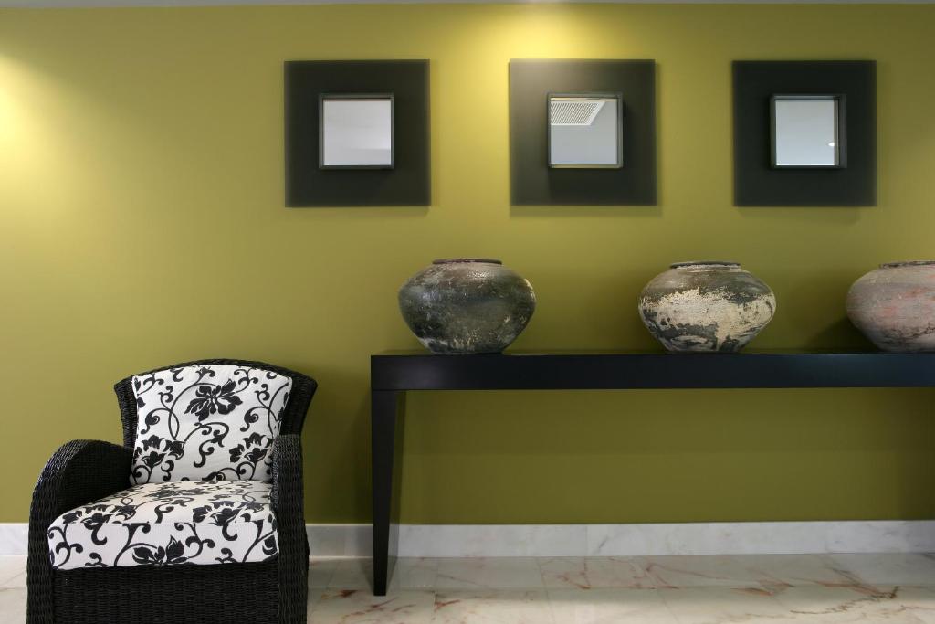 Mūsdienīgs interjers ar melnu krēslu un dekoratīvām podiņiem uz melnas plaukta, fona krāsa ir gaiši zaļa.