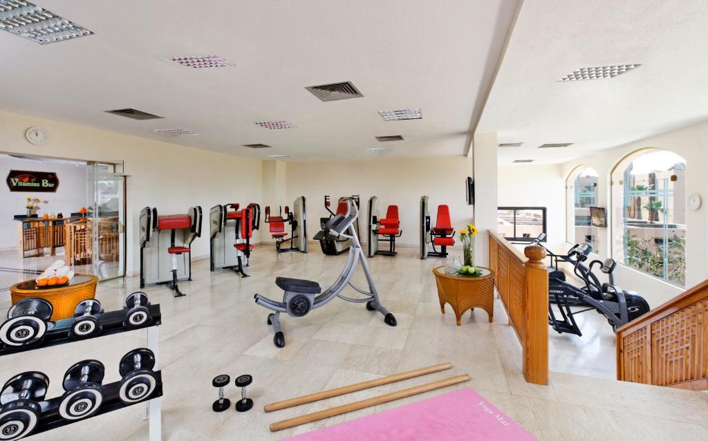 Moderns sporta zāles interjers ar dažādām trenažieru iekārtām, hantelēm un vitamīnu bāru fonā. Lielie logi nodrošina dabisko apgaismojumu, radot patīkamu atmosfēru.