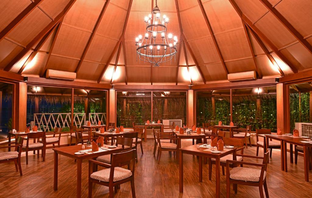 Eleganta restorāna iekārtojums ar koka mēbelēm un modernu apgaismojumu, kas rada siltu atmosfēru. Lielie logi nodrošina skatu uz zaļo apvidu, piešķirot vietai īpašu šarmu.