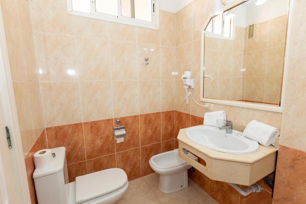 Moderns vannas istabas interjers ar viegliem krēmveida un oranžiem flīžu toņiem, iekļaujot izlietni, toleti un spoguli. Vannas istaba ir labi apgaismota un kārtīga.