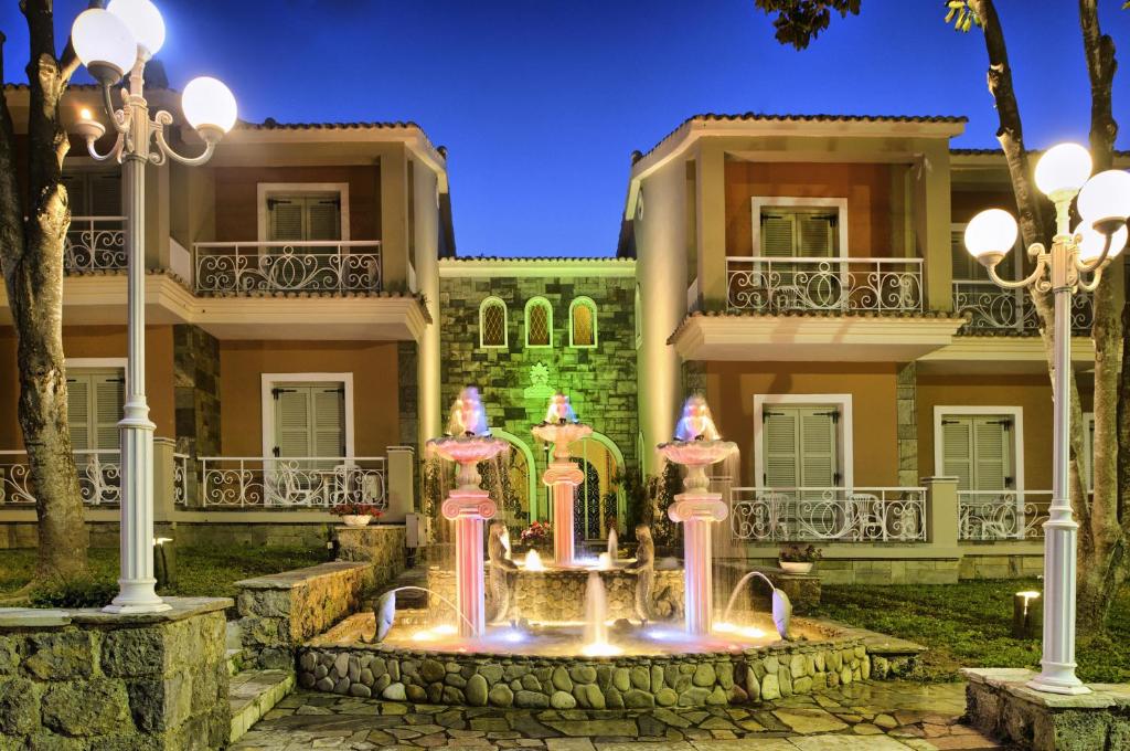 Ainava ar strūklaku un apgaismojumu, kas atrodas viesnīcas kompleksa priekšā, radot burvīgu atmosfēru vakarā. Viesnīcas arhitektūra apvieno modernus un tradicionālus elementus.