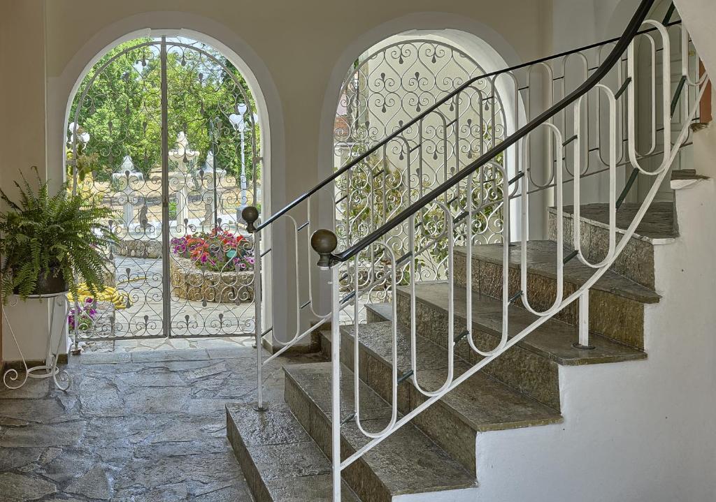 Eleganta kāpnes ar metāla margām, kas ved uz dārzu ar krāšņiem ziediem un strūklakām. Svaiga un gaisīga telpa, kas rada mierīgu atmosfēru.