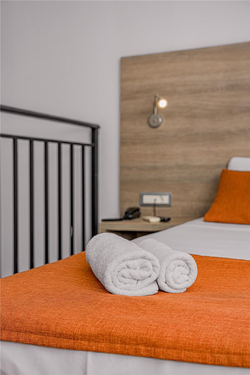 Tīri, sarullēti dvieļi uz gultas Panorama Village Hotel numurā, akcentējot tīrību un kārtību