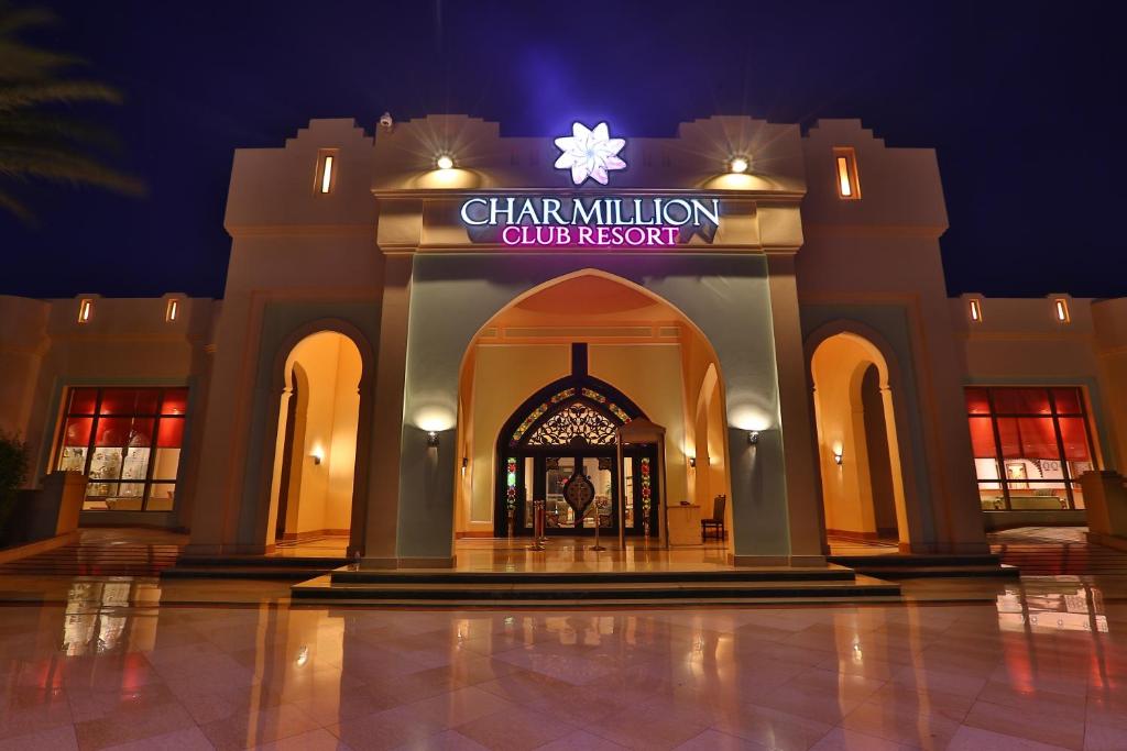 Charmillion Club Resort ieejas durvis nakts apgaismojumā, ar elegantu arhitektūru un modernām detaļām. Viesnīcas nosaukums redzams virs ieejas, radot pievilcīgu atmosfēru.