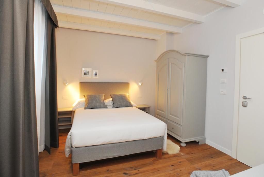 Moderns guļamistabas interjers ar gultu, pelēkiem aizkariem un koka grīdu. Telpā ir gaismas avoti un skapītis.