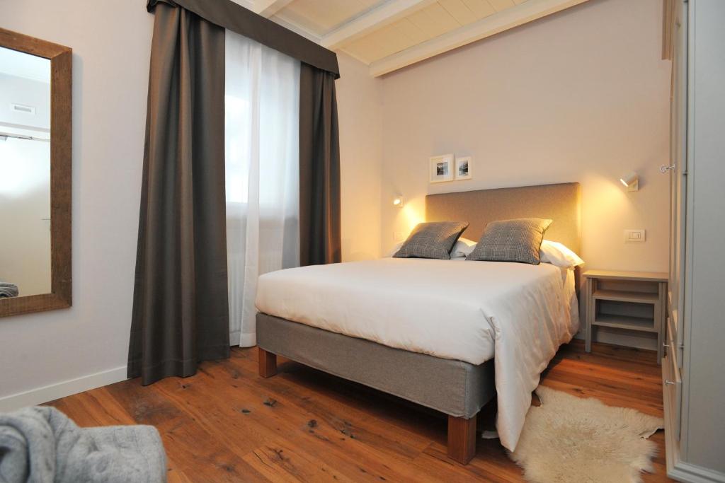 Mūsdienīga guļamistaba ar divguļamo gultu un koka grīdu, apgaismota ar siltām gaismām. Logi ar viegliem aizkariem un stilīgs spogulis papildina telpas estētiku.