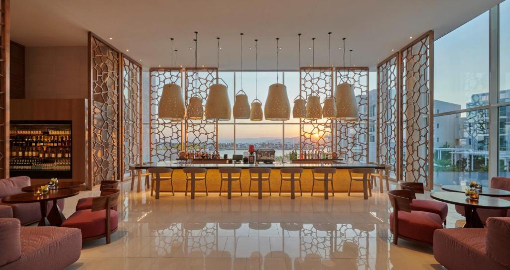 Mūsdienīgs bārs ar elegantu apgaismojumu un panorāmas logiem, caur kuriem redzams saulriets. Interjers apvieno modernu dizainu un komfortu, piedāvājot relaksējošu atmosfēru.