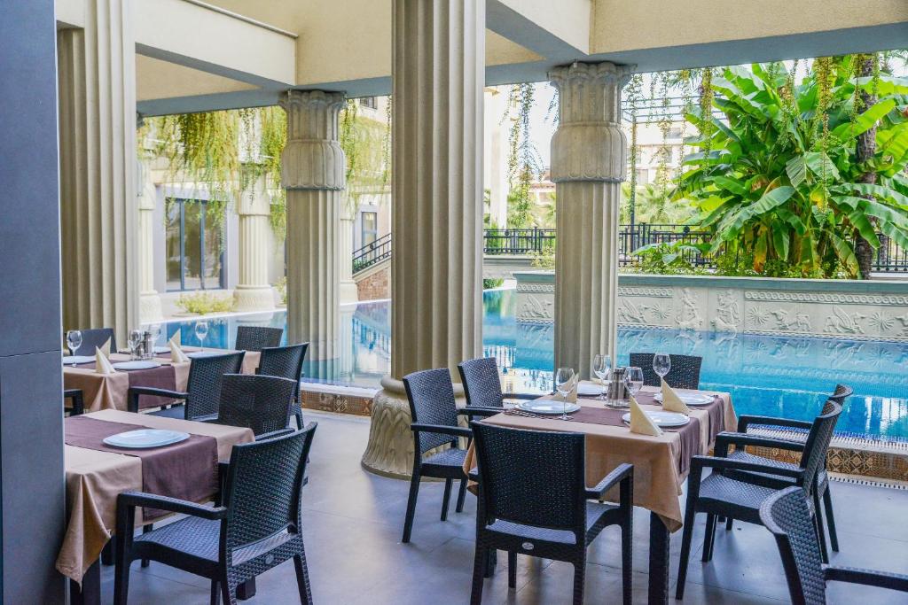 Restorāna terase ar skatu uz baseinu un zaļām palmu lapām, kā arī eleganti klāti galdi.