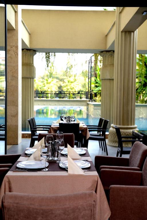 Elegants restorāns ar skatu uz baseinu, kur galdi ir klāti ar galdautiem un galda piederumiem, radot izsmalcinātu atmosfēru. Daba un arhitektūra harmoniski saplūst, piedāvājot relaksējošu vidi.