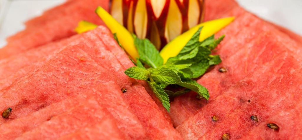 Svaiga, sagriezta arbūza daļa ar piparmētru un augļu rotājumu, kas piešķir krāsainību un svētku noskaņu.