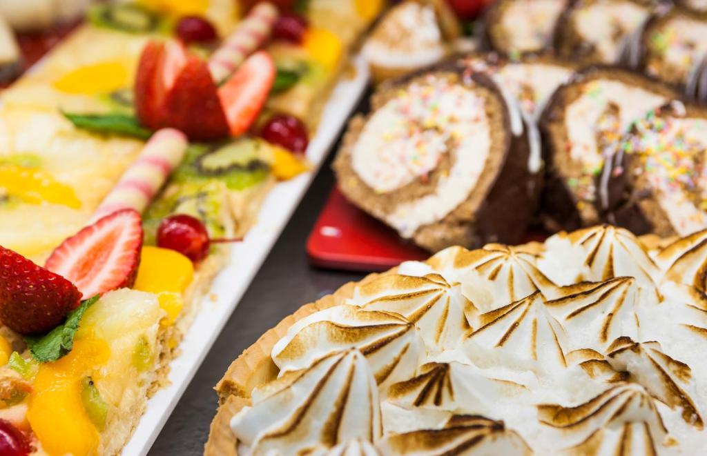 Krāsainu desertu plāksne ar augļu kūku, šokolādes ruletēm un meringue pīrāgu. Dekorēti ar svaigiem augļiem un krāsainām konfektēm.