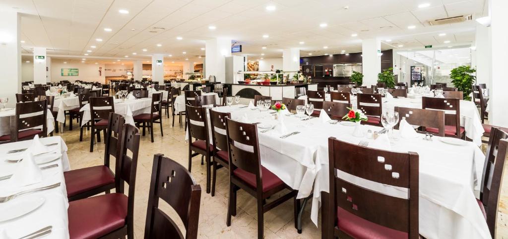 Restorāna iekšskats ar daudziem galdiem, kas klāti ar baltām galdautām un galda piederumiem, gatavi viesiem. Moderns dizains un plaša telpa rada patīkamu atmosfēru.