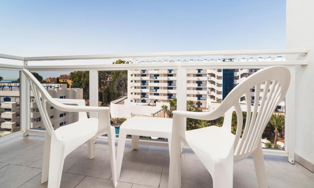 Balkons ar divām baltām plastmasas krēsliem un galdu, skats uz apkārtējiem ēkām un zaļumiem. Ideāla vieta relaksācijai.