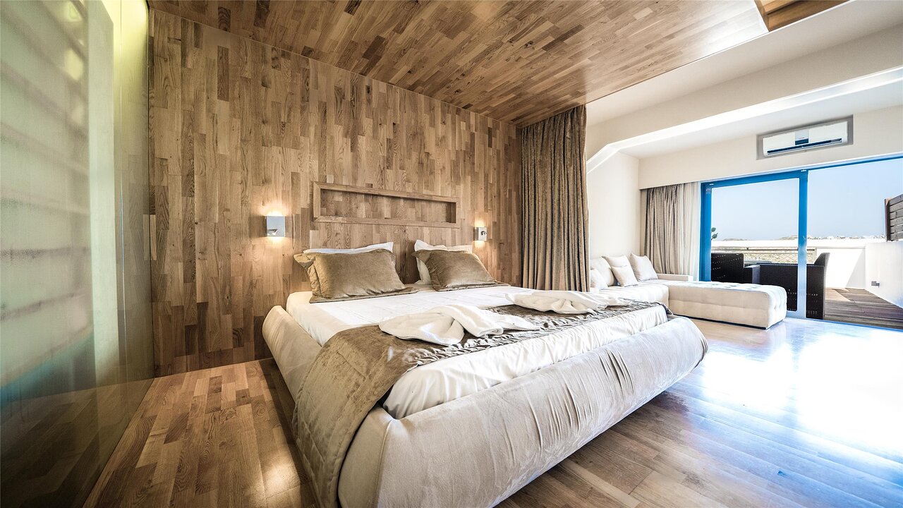 Moderns Panorama Village Hotel numurs ar koka apdari, plašu gultu un izeju uz saulainu terasi.