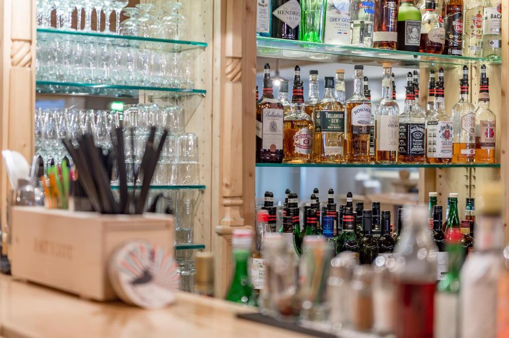 Bāra plauktā redzamas dažādas alkoholiskās dzērienu pudeles un glāzes, kā arī bāra piederumi. Ideāla atmosfēra dzērienu baudīšanai.