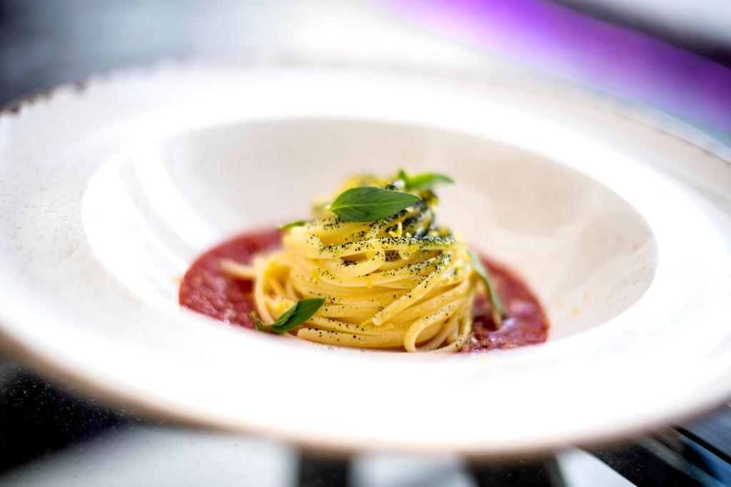 Pasta ar tomātu mērci un svaigiem bazilika lapām, pasniegta elegantā traukā.