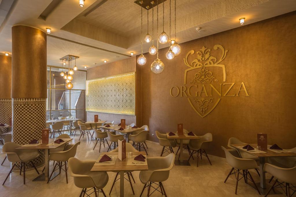 Mūsdienīga restorāna interjers ar elegantu apgaismojumu un gaumīgu dekoru, uz sienas redzams zelta "Organza" logo. Galdiņi ir sakārtoti ar stilīgām ēdienkartēm un akcentiem.