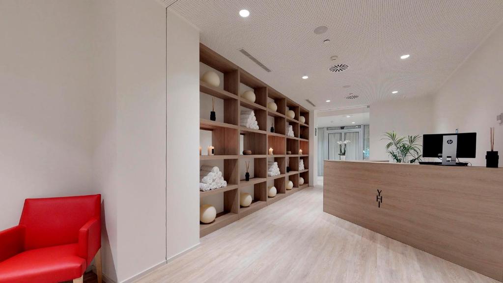 Mūsdienīgs un elegants reģistratūras interjers ar sarkano krēslu, koka plauktiem un neitrālām krāsām, radot viesmīlīgu atmosfēru.