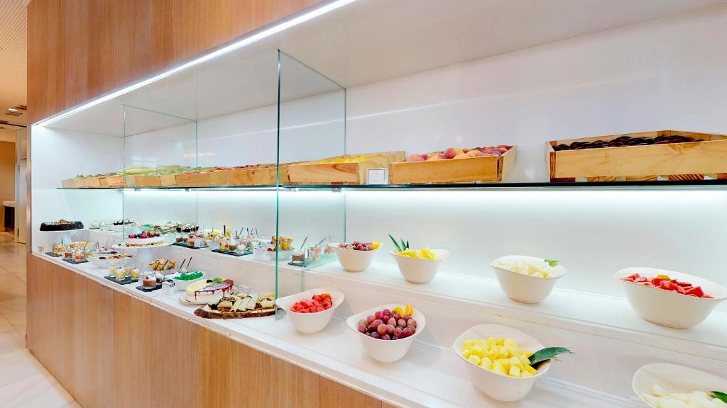 Svaigu augļu un desertu bufete ar dažādām kārumiem, kas izvietoti stikla plauktos un traukos, nodrošinot pievilcīgu un krāsainu piedāvājumu.