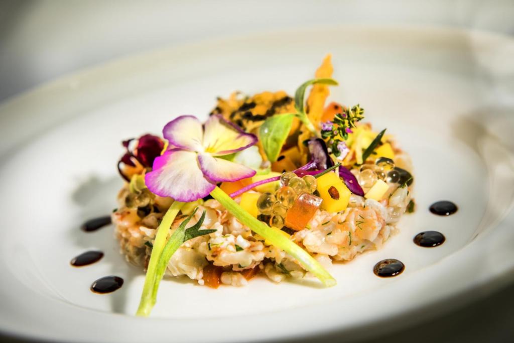 Gurķu un ziedu dekorēta rīsu uzkoda ar garnelēm un mango, pasniegta eleganti uz balta šķīvja.