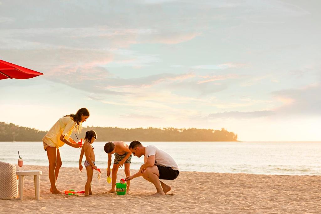 Ģimene spēlē pludmalē pie Angsana Laguna Phuket, saulriets.