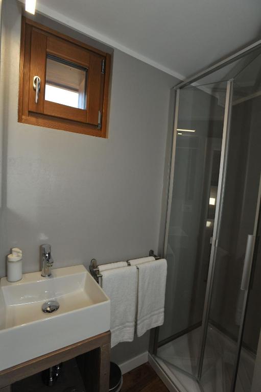 Mūsdienīgs vannas istabas interjers ar dušas kabīni, izlietni un koka logu. Balti dvieļi un higiēnas piederumi pieejami uz plaukta.