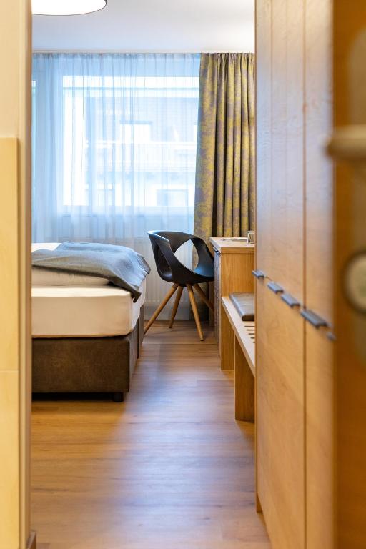 Mūsdienīgs viesnīcas numurs ar gaisīgu interjeru, kas ietver gultu, rakstāmgaldu un ērtu krēslu, izgaismots ar dabiskiem saules stariem caur logu.