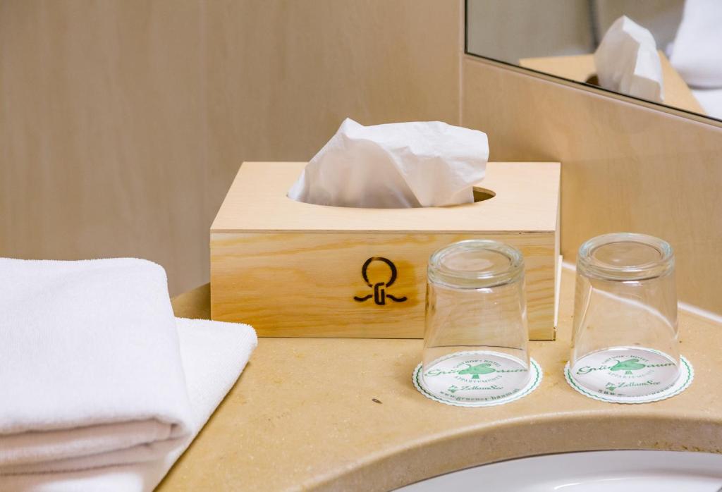 Koka auduma kastīte ar salvetēm un divi glāzītes uz vannas istabas izlietnes, blakus dvieļiem un košiem.