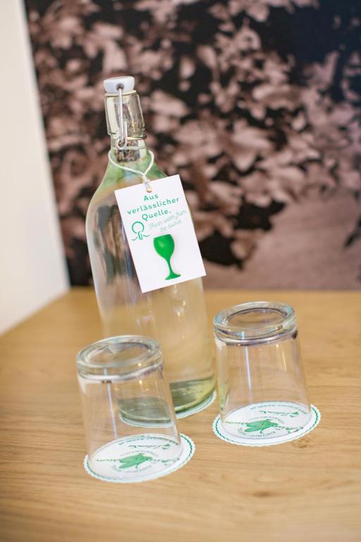 Stikla pudele ar etiķeti un divi apgriezti glāzes uz koka galda, fonā redzama melnbalta ainava.