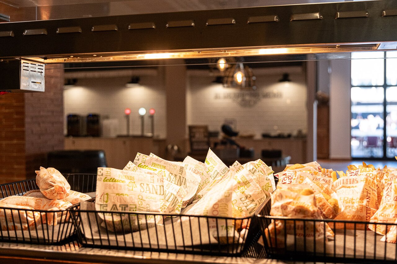 Sviestmaizes un uzkodas papīra iepakojumos metāla grozos zem sildlampām Estival Park Marena bufetē